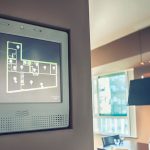 Wandmontiertes Smart-Home-Display zeigt den Grundriss einer Wohnung mit vernetzten Geräten und Lichtsteuerung in einem modernen Wohnraum. | Immobilienbewertung