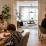 Familie im Homeoffice: Eine Frau arbeitet am Laptop am Esstisch, während ein Kind daneben Hausaufgaben macht und ein Mann in einem separaten Arbeitsbereich telefoniert. I Homeoffice-Boom